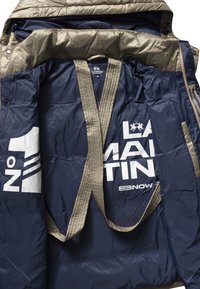 Námořnická modrá zateplená bunda se světle hnědým podšívkou, s velkým bílým logem a popruhy uvnitř, navržena pro teplo a pohodlí.