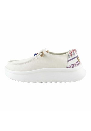 Zapatilla de lona blanca sin cordones con suela blanca gruesa y acento estampado en el talón. Presenta un regulador de cordones para un ajuste seguro.