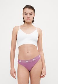 Bílý bavlněný bralet s tenkými ramínky, v kombinaci s růžovými bikinovými spodními kalhotkami s logem na pásku. Hladký, přiléhavý design.