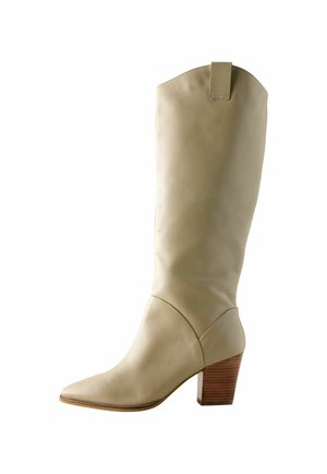 Stivale in pelle beige alto fino al ginocchio con punta affusolata e tacco a blocco in legno. Presenta una texture liscia e una linguetta nella parte superiore per facilitare l'indossamento.