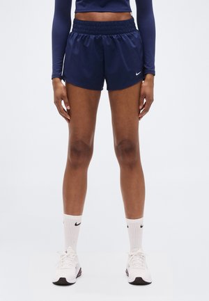 Donkerblauwe sportshorts met een elastische tailleband, gemaakt van lichtgewicht stof, gecombineerd met witte Nike-sokken en sneakers.