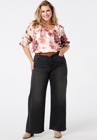 Bloemenblouse met geruite mouwen, gecombineerd met een hooggetailleerde, wijduitlopende donkere spijkerbroek en een bruine riem. Beige schoenen maken de outfit compleet.