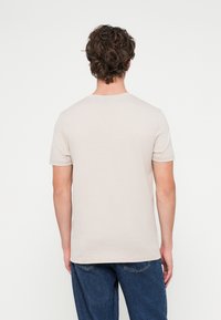 Μπεζ βαμβακερό t-shirt με κοντά μανίκια, στρογγυλή λαιμόκοψη και ίσια τελείωμα, φορεμένο από άτομο που φαίνεται από την πλάτη.