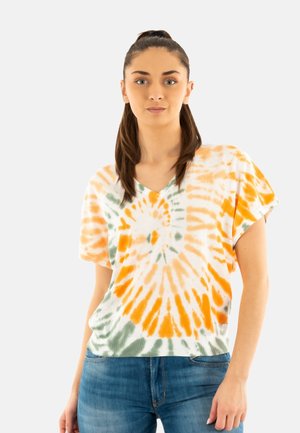 Top à manches courtes, col en V, en tie-dye blanc, orange et vert, avec un motif tourbillonnant et une coupe décontractée, associé à un jean bleu.
