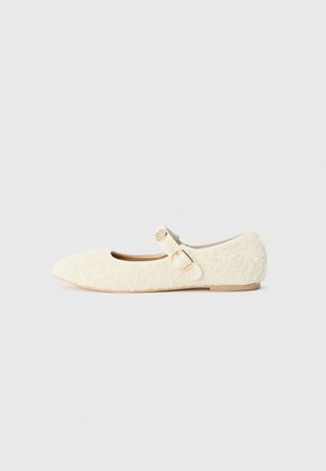 Cream-colored ballet flat made of textured fabric. Features a rounded toe and a small side buckle fastening. Flat sole.
