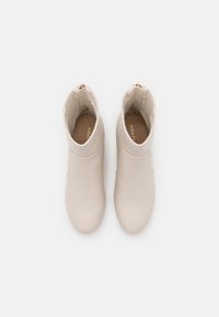 Beżowe botki za kostkę wykonane z gładkiej skóry, z okrągłym noskiem, bocznym zamkiem błyskawicznym i teksturowaną podszewką wewnątrz.