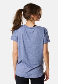 T-shirt bluette a maniche corte con vestibilità rilassata, texture morbida e scollo tondo, indossato sopra un top sportivo nero.
