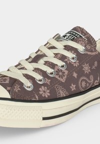 Παπούτσι Converse χαμηλό με κρεμ κορδόνια, καφέ σχέδιο paisley και floral, λευκή ελαστική σόλα και μαύρη λεπτομέρεια ρίγας.