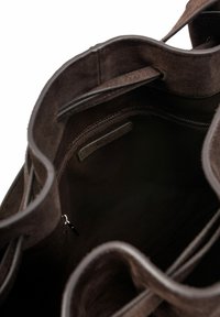 Wnętrze brązowej torby typu tote zamszowej, z teksturowaną tkaniną, otwartą górą z zaokrąglonymi krawędziami i małą kieszenią na suwak.