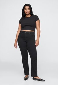 Črna pristrižena majica s kratkimi rokavi, združena z visokim pasom črnih kavbojk. Model nosi črne balerinke. Enobarvno ozadje.