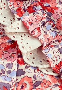 Tessuto floreale con fiori rosa, rossi e viola e rifiniture in pizzo bianco. Il design include volants e una texture morbida.