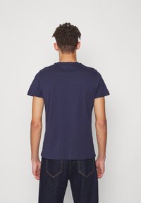 Námorně modré bavlněné tričko s krátkými rukávy, kulatým výstřihem a hladkým povrchem, nošené s tmavými džínami, z pohledu ze zad.