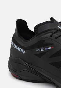 Czarne buty sportowe z teksturowaną cholewką, wzmocnionym zapiętkiem i szarymi akcentami logo. Posiadają elegancki, niski krój oraz elastyczną podeszwę.