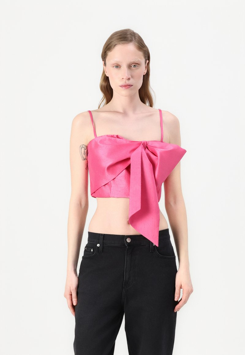 Rosa satin crop top med tunna band och en stor framknutning, kombinerat med svarta högmidjade jeans; slät textur och livfull färg.