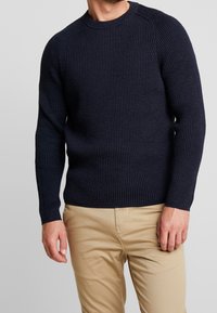 Maglione a coste navy con maniche lunghe e design a collo rotondo, caratterizzato da una finitura testurizzata e una vestibilità aderente, abbinato a pantaloni khaki.