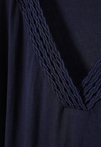 Tissu bleu foncé avec une bordure tressée texturée formant un V au niveau de l'encolure du vêtement.