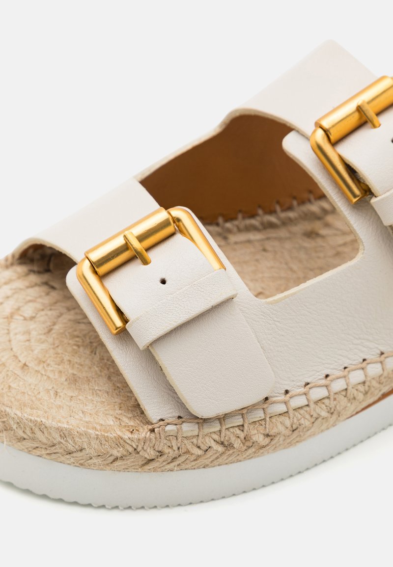 Weiße Leder-Sandaletten mit goldener Hardware, offenem Design, jute-umwickelter Sohle und strukturiertem Stichdetail entlang der Kante.