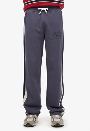 Navy blue sweatpants with contrast side stripes, drawstring waist, and "Superdry Athletics" logo. Soft material, relaxed fit, full-length.