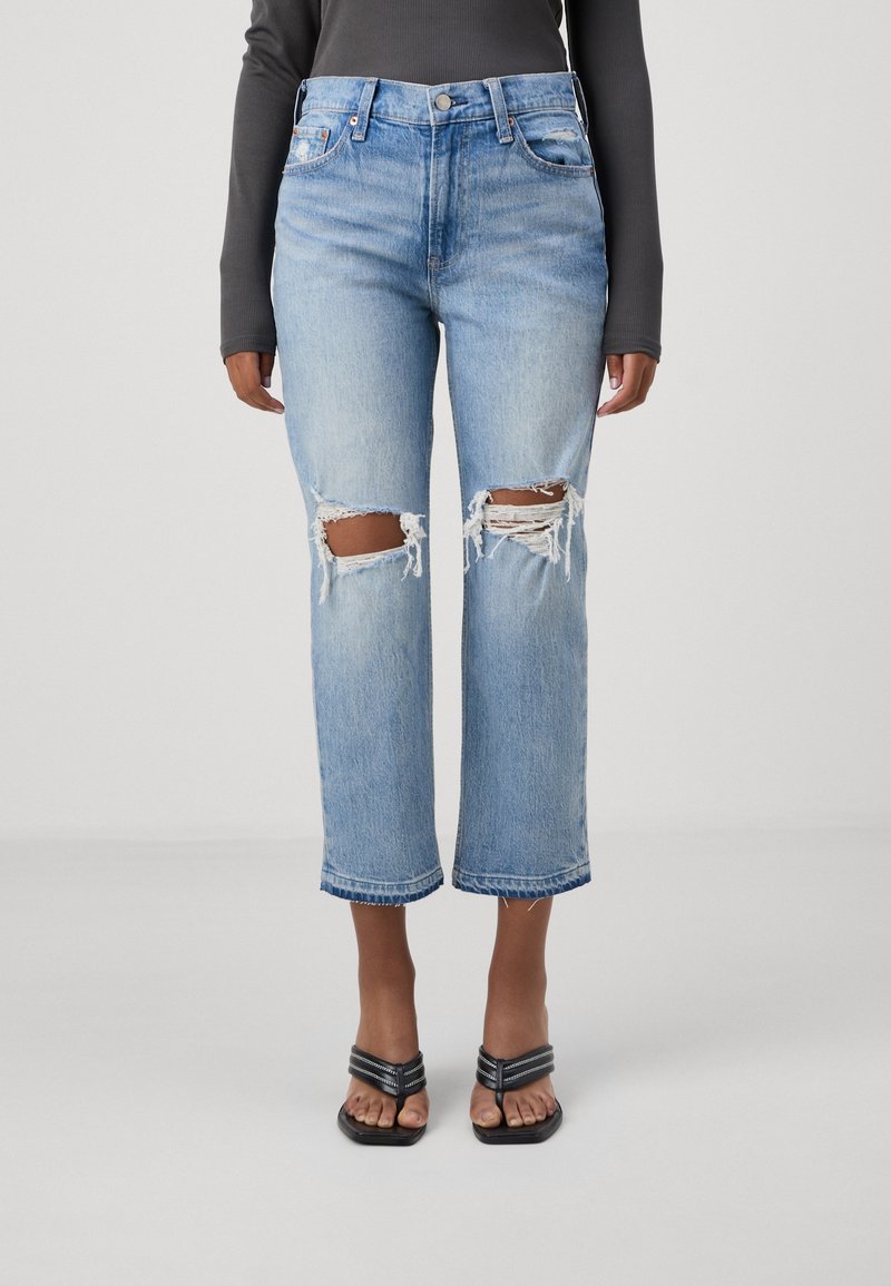 Světlé modré modelované džíny s roztrhanými koleny, uvolněný střih, zkrácená délka a rozfrcaný lem. V páru s černými sandály na páskách.