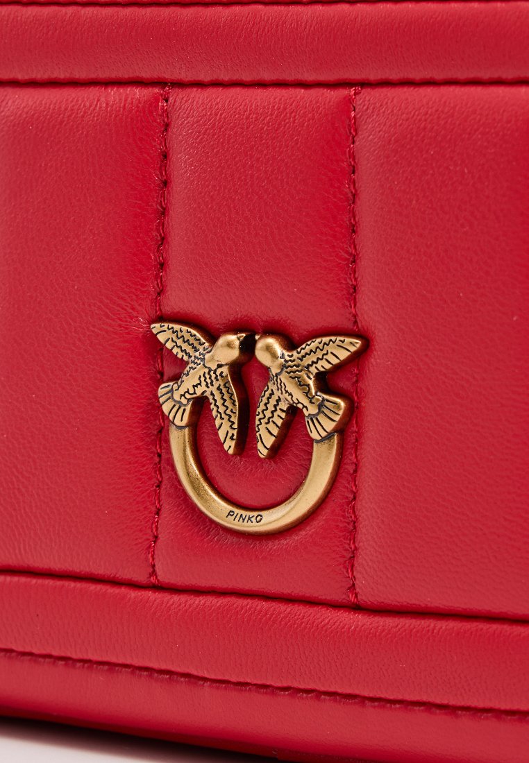 Sac à main en cuir rouge avec un accent en métal doré, présentant deux motifs d'oiseaux entrelacés autour d'un anneau. Finition texturée et détails cousus.