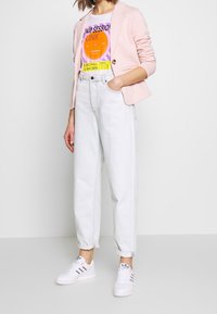 Ljust rosa kavaj, grafisk T-shirt i lila, orange och gult, högmidjade ljusa jeans och vita sneakers med färgade ränder.