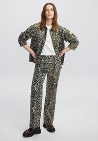 Set di giacca e pantaloni con stampa leopardata in toni tenui di beige e nero. Design informale con bottoni e tasche, abbinato a una t-shirt bianca.