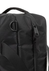 Sac à dos en tissu noir avec une surface texturée, fermeture éclair, poignée supérieure et bandoulière réglable, avec une construction durable.