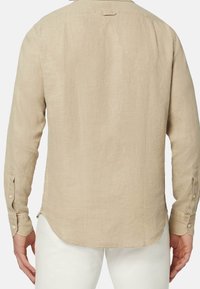 Camisa de lino beige de manga larga con un dobladillo curvado, puños abotonados y un detalle de yugo en la parte posterior, que muestra una tela texturada.