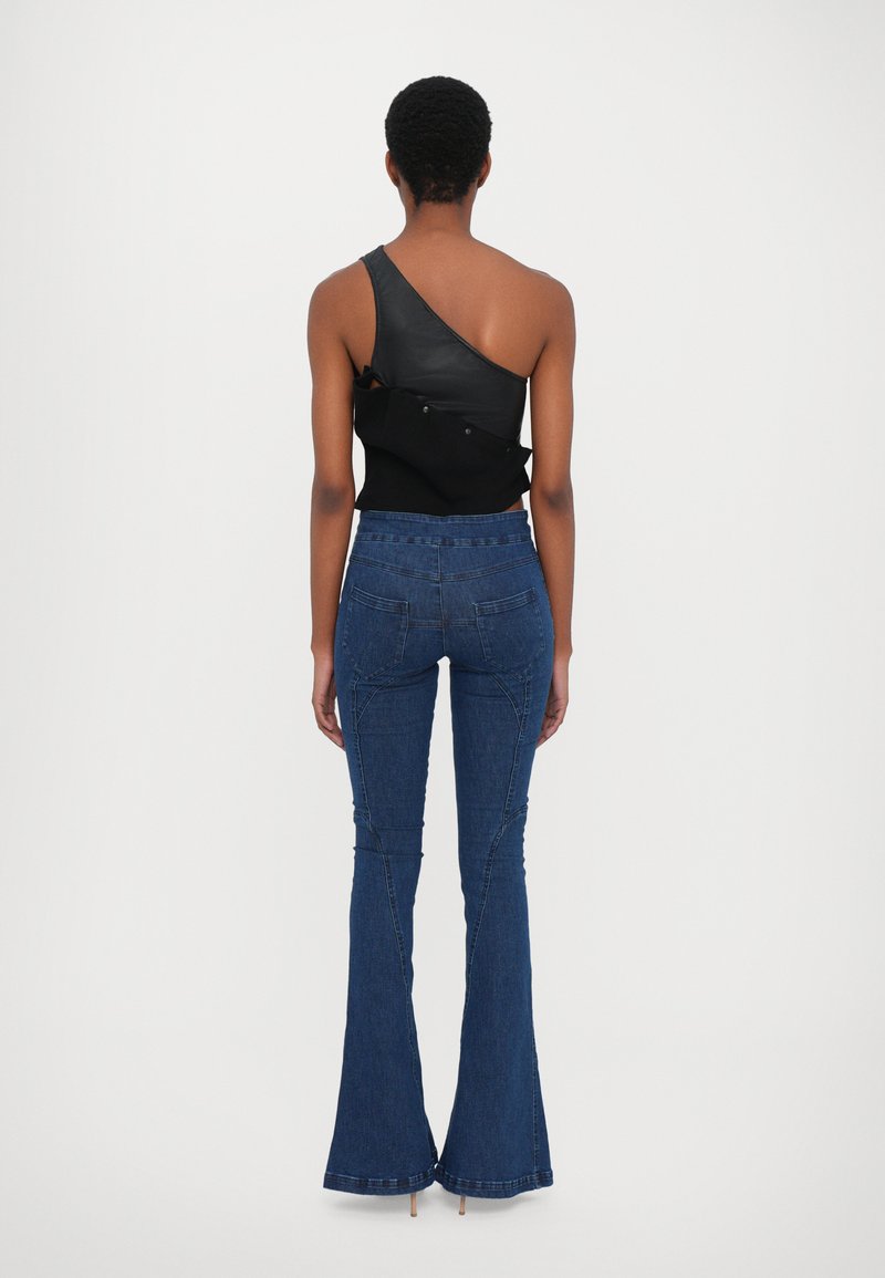 Svart enaxlad topp i läder och tyg, matchad med högmidjade blå vida jeans med sömnadsdetaljer och framsidofickor.