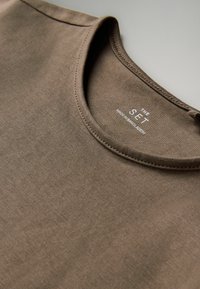 Brązowy bawełniany T-shirt z okrągłym dekoltem i gładką teksturą, subtelnymi przeszyciami oraz metką "THE SET" wewnątrz kołnierza.