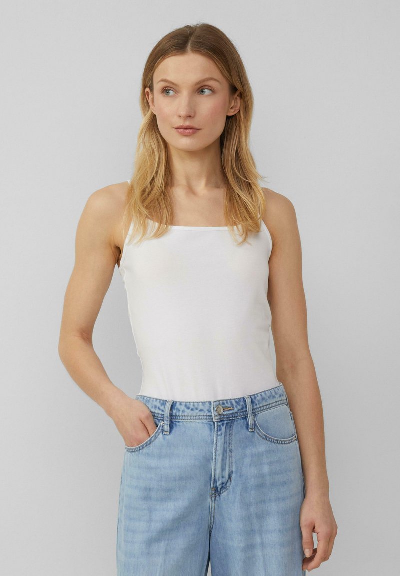 Weißes, eng anliegendes Tanktop mit schmalen Trägern und quadratischem Ausschnitt. Kombiniert mit hellblauen, hochgeschnittenen Jeans. Einheitliche Textur, keine Muster.