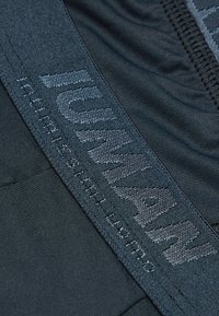 Černé boxerky z elastické látky s texturovaným pasem, na kterém je embossovaný nápis "HUMAN." Hladký povrch a bezešvá konstrukce.