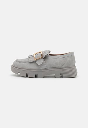 Mocassins en daim gris avec une semelle en caoutchouc épaisse et un détail de frange décoratif, featuring une boucle en métal doré sur le dessus.