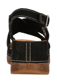 Svarta mockasandaler med justerbar rem, tan vadderad fotbädd och strukturerad brun sula. Sonderingsdetalj ger kontrast till designen.