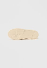 Podeszwa kremowo-białego buta sportowego z bieżnikiem w jodełkę i logo "Tommy Hilfiger" wytłoczonym na gumowej podeszwie zewnętrznej.