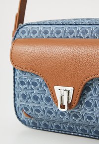 Borsa a tracolla in tessuto blu con motivo, dotata di una patta in pelle marrone e accessori in argento. Presenta un design testurizzato unico e un motivo geometrico.