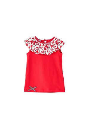 Haut rouge avec col volanté à motif de cœurs, associé à un pantalon blanc à pois noirs et bordure rouge festonnée ; sandales rouges.