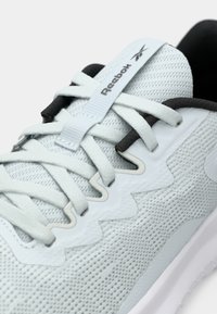 Pantofii sport de culoare albastru deschis au un superior din plasă, accente texturate, șireturi plate și un interior negru contrastant. Prezintă brandingul Reebok pe limbă.