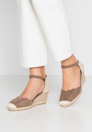 Sandalias cuña espadrille color topo desgastado con borde ondulado, correa en el tobillo y punta blanca, combinadas con pantalones cortos blancos.