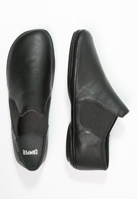 Zapatos negros de piel sin cordones que cuentan con paneles elásticos en los laterales, puntera redondeada y textura suave. Diseñados para ofrecer comodidad y facilidad de uso.