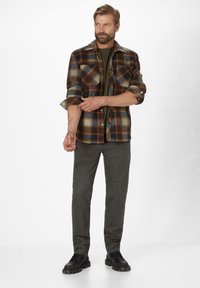 Flannel shirt in brown, blue, and orange plaid; features button-up front and two chest pockets. Paired with grey pants and black shoes.