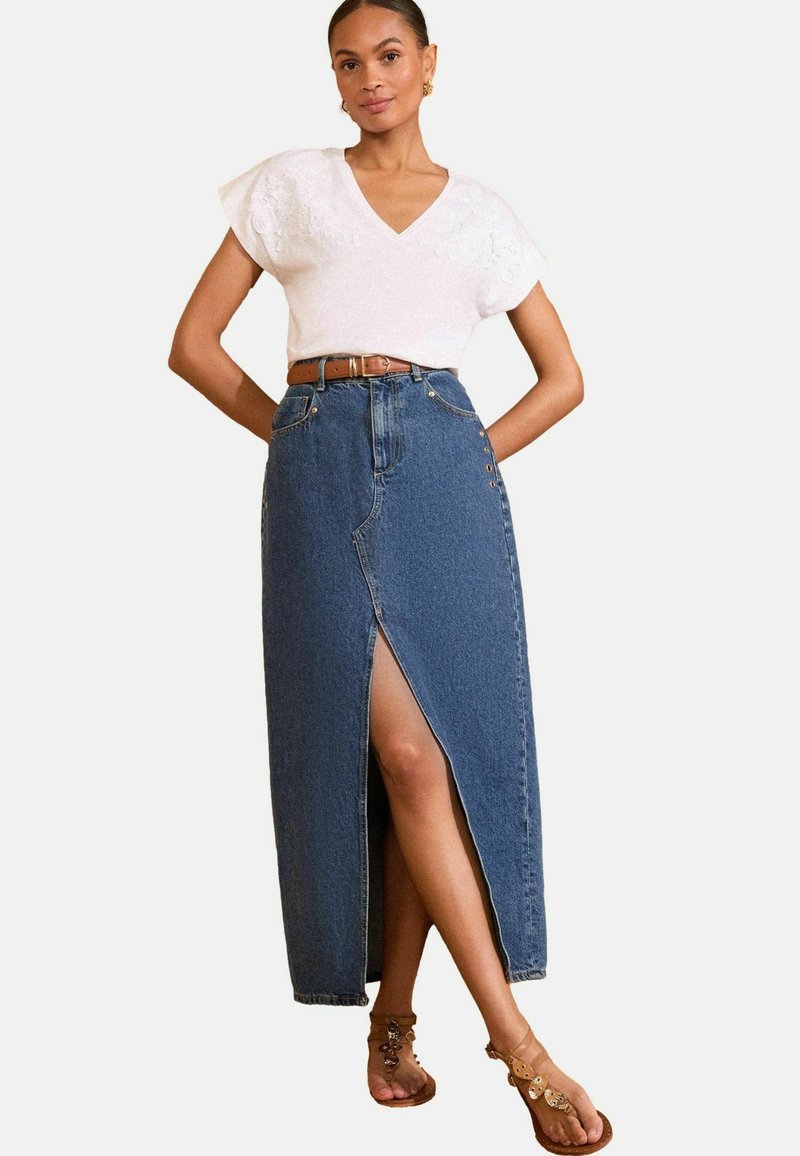 High-waisted, front-slit denim skirt in dark blue with buttons on the side, paired with a white V-neck top and a brown belt.