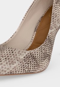 Gros plan sur un escarpin pointu beige et marron à motif peau de serpent avec une semelle intérieure matelassée couleur tabac.