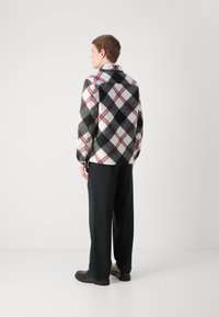 Black, white, and red plaid fleece jacket with a collar and long sleeves; model wearing loose black trousers and black shoes.