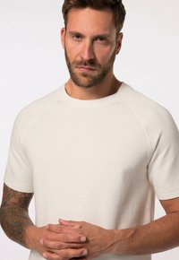 Camiseta de cuello redondo en beige claro con mangas cortas tipo raglán, hecha de una suave tela de mezcla de algodón. Presenta detalles de costura sutiles.