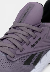 Ténis Reebok com um upper de tecido roxo, atacadores cinzentos e acabamentos em preto. Apresenta um design de rede respirável e sola acolchoada.