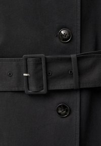 Gros plan sur un tissu noir avec deux boutons noirs et une ceinture assortie avec une boucle rectangulaire et une épingle métallique.