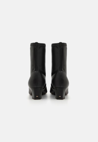 Botine negre din piele cu toc scurt, având o textură netedă, detalii cu cusături verticale și un accent simplu de aur pe toc.