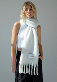 Lichtgrijze sjaal van zacht materiaal met franjes aan de randen. Heeft een label met "ARCTIC FOX" aan één kant. Om de hals gedragen.