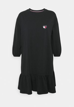 Vestido negro de longitud a la rodilla con largas mangas de globo, dobladillo con volantes y un pequeño detalle de corazón bordado en el pecho. Fabricado en tela suave.